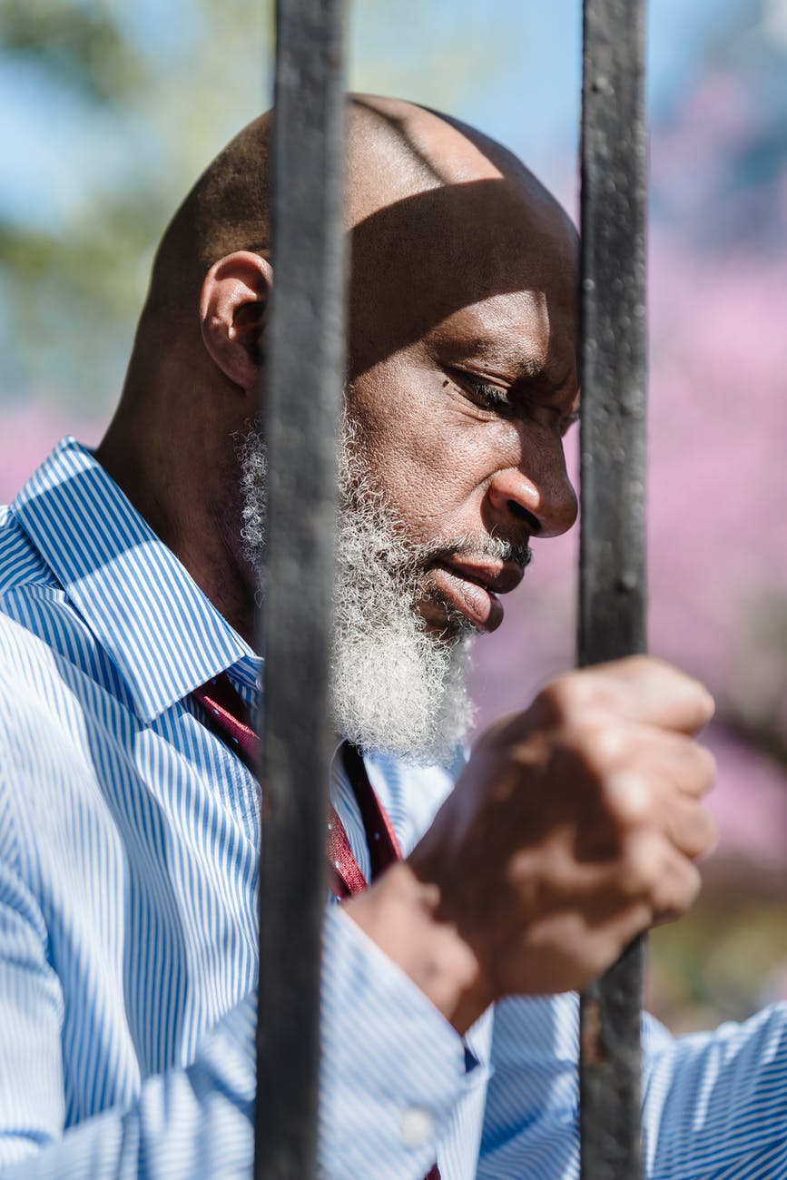 stressed black man gripping metal fence bars in daytime