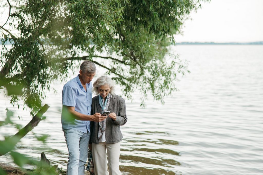 elderly couple looking at the smartphone standing near the body of water