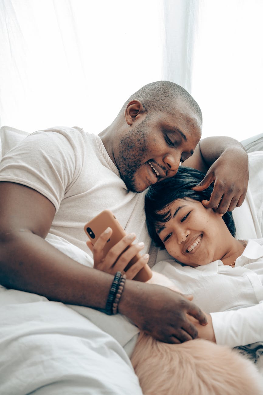 cuddling multiracial spouses watching video on smartphone lying in bed