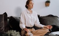 woman in white button up long sleeve shirt sitting on black couch in lotus position